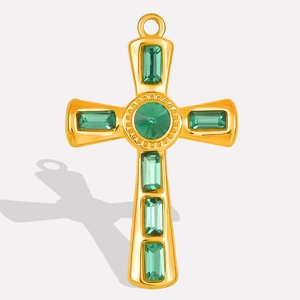 Detailed shot of a gold cross pendant with green stones and a top hanging ring