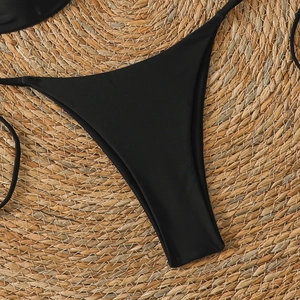 Flat lay detail of black string bikini bottom on natural straw background