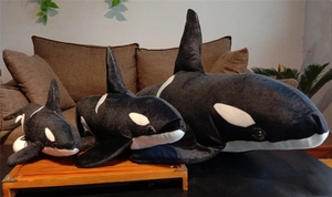 Three plush orca toys in different sizes arranged together on a wooden table decoration