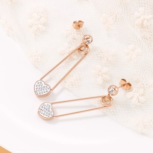 Détail de boucles d'oreilles cœur et trombone en or rose avec strass blancs brillants