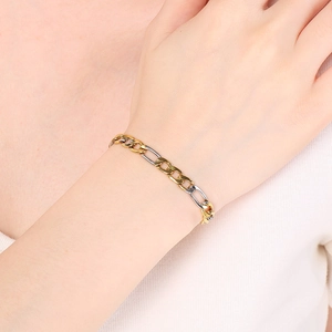 Detail of bicolor gold and silver stainless steel Figaro chain bracelet on model's wrist