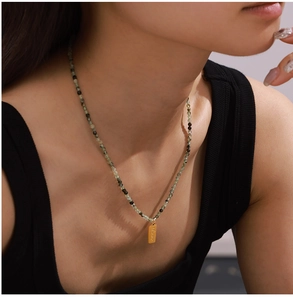 Detail of beaded necklace with green natural stones and gold Love pendant on a model
