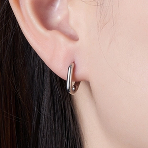 Macro shot of a minimalist silver U-shaped earring on a model's ear showing polished finish