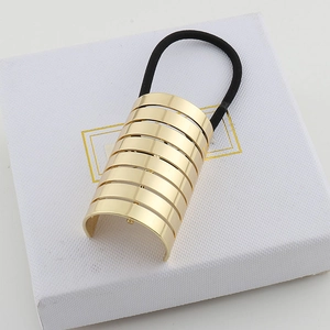 Close-up of golden striped metal hair cuff with elastic band on a white textured box