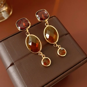 Dettaglio di orecchini vintage con gemme in vetro bordeaux e ambra su base in pelle