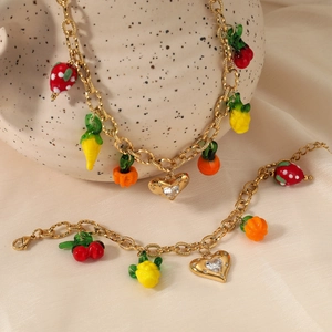 Golden fruit charm necklace and bracelet set displayed on silk and ceramic vase