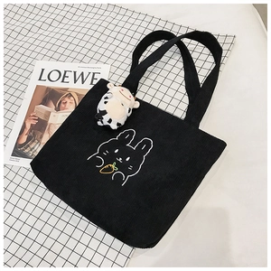 Detail of black corduroy tote bag with white bunny embroidery and cow plush charm