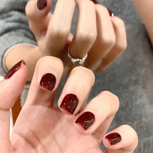 Detail of glossy deep red press-on nails with shiny mirror finish and silver ring