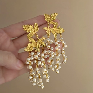 Macro shot of long gold leaf earrings with white pearl tassels held by a hand