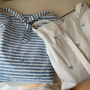 Détail de sacs fourre-tout en coton rayé bleu et beige avec broderies de nœuds souples
