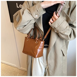 Sac seau en cuir marron brillant à poignées nouées porté avec un trench-coat beige