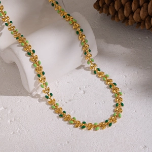 Detailed close-up of 18K gold plated leaf necklace with green enamel on white background