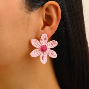 Detail shot of large pink raffia woven flower earrings with textured petals on model