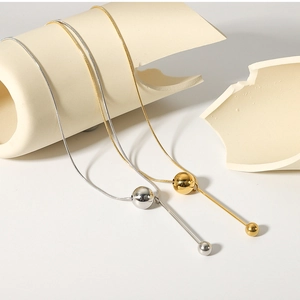 Close-up of gold and silver snake chain necklaces with spherical and long bar pendants
