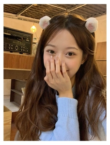 Close-up of white plush ear hair clip accessory worn by a girl in a cozy indoor setting