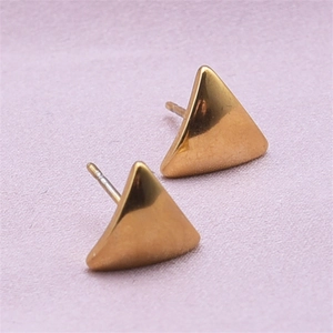 Macro shot of polished gold triangular stud earrings on a textured pastel background