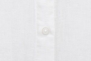 Close-up of white linen fabric texture with a translucent button on long sleeve shirt