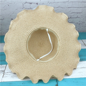 Detail of light beige straw hat featuring wavy scalloped brim and elastic chin strap