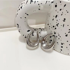 Macro view of polished silver U-shape hoop earrings against a white ceramic textured cup