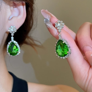 Macro detail of pear-shaped emerald green drop earrings with intricate crystal floral studs