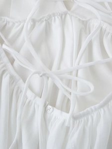 Detail of white dress featuring tie-back design, single button, and pleated fabric texture