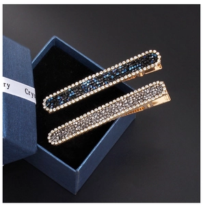 Detail shot of two gold-plated hair clips with inlaid rhinestones on a blue jewelry box