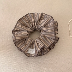 Gros plan du chouchou à rayures marron avec une étiquette nœud tissée sur un fond en tricot doux