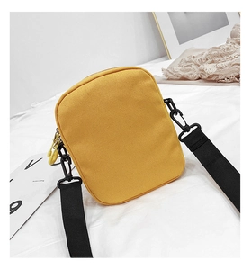 Detail of yellow canvas crossbody bag showing texture, black strap, and zipper pull