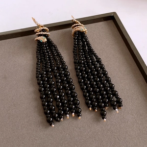 Detail view of long black beaded tassel earrings with gold crystal snake head accents