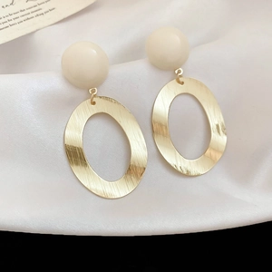 Close-up of golden brushed metal oval earrings with cream resin studs on white silk fabric