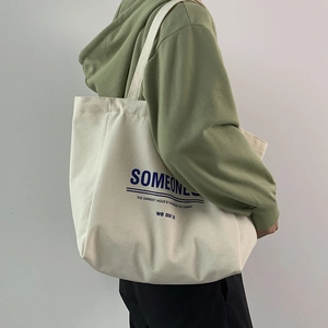 Detail of off-white canvas tote bag with blue lettering and green outfit on model