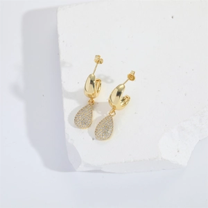 Elegant gold teardrop earrings with pavé crystals on a minimalist stone background
