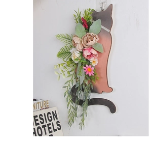 Detailed view of cat-shaped wooden wreath with pink peonies and green leaves on white wall