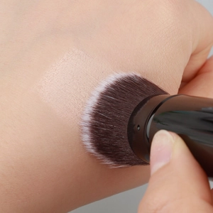 Macro view of synthetic bristles applying liquid foundation smoothly on skin texture