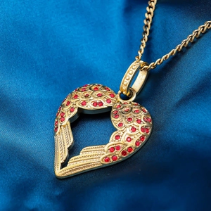 Collana con cuore e ali d'angelo dorata con cristalli rossi su sfondo di seta blu