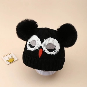 Détail du bonnet tricoté pour bébé avec motif hibou et deux grands pompons moelleux