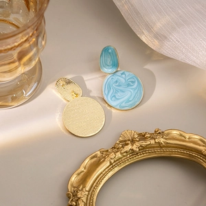 Detailed close-up of sky blue marble texture earrings with golden geometric round metal base
