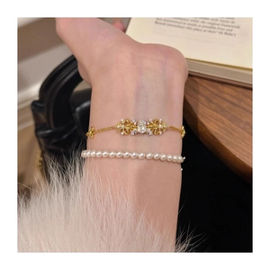 Close-up of stacked gold fleur-de-lis chain bracelet and elegant pearl bead bracelet
