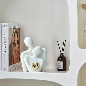 Modern abstract ceramic couple sculpture with gold heart decor on a white shelf