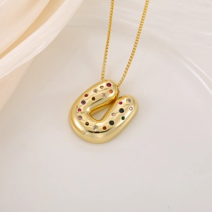 Detail shot of a puffy 18K gold letter U pendant with multi-colored zircons on silk