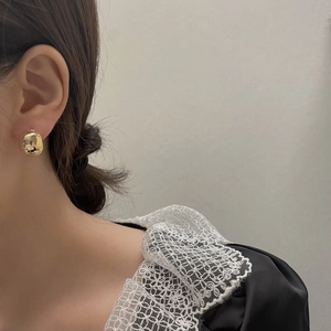 Dettaglio di eleganti orecchini a bottone dorati indossati da una modella con stile chic