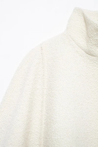 Close-up detail of white knitted stand-collar sweater showing soft textured fabric material
