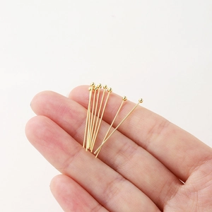 Close-up of gold ball head pins for jewelry making held in hand for size reference