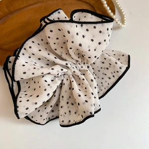 Detailed view of a white polka dot hair scrunchie with elegant black ruffled lace edges