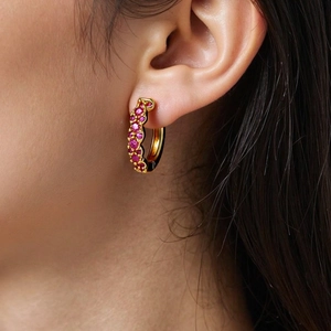 Close-up of gold hoop earring with pavé-set pink cubic zirconia on a model ear