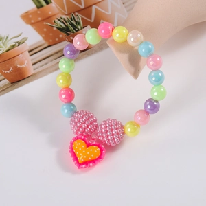Close-up of colorful beads and pink polka dot heart charm on a children's beaded bracelet