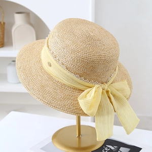 Detail of straw hat featuring a yellow chiffon bow, white lace edge and gold brand plaque