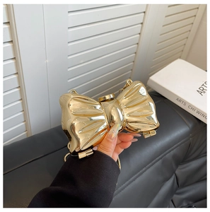 Detailed close-up of a gold metal bow clutch with chain strap held by a model