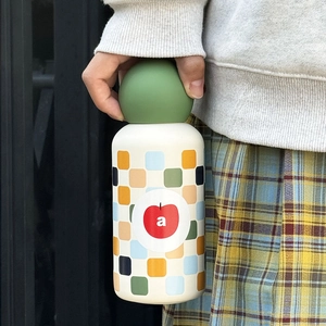 Detail of creative cream water bottle with green lid and apple design held by person