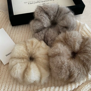 Three plush faux mink fur scrunchies in cream and brown on a knit background